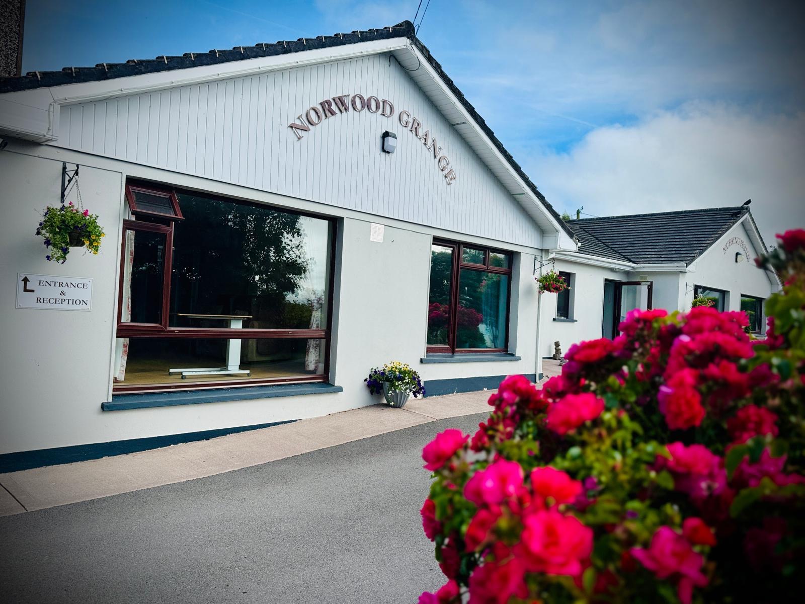 The entrance and reception of Norwood Grange, with hanging baskets and roses by the path